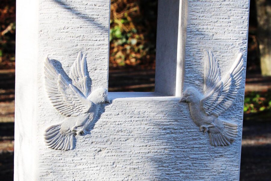 Heller Gedenkstein mit Fenster und zwei Tauben