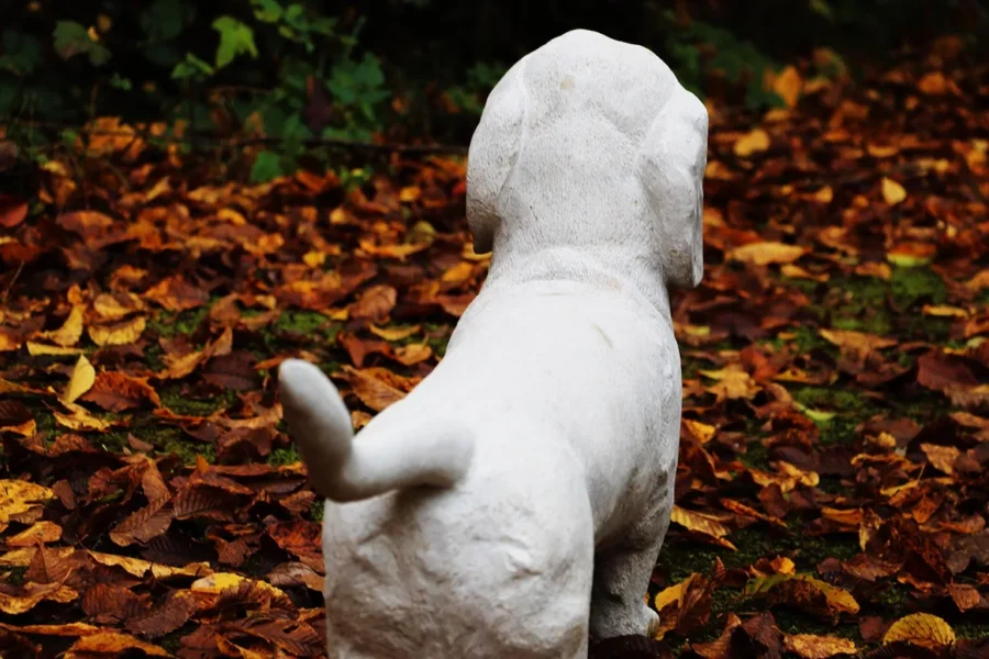 Hundefigur aus hellem Stein im Herbstlaub